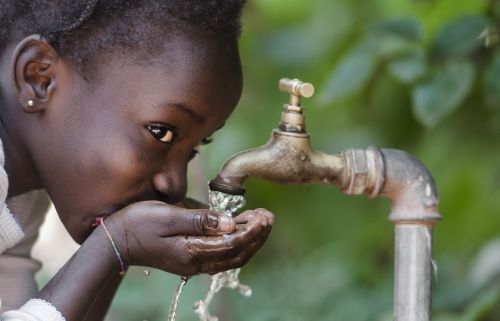 een meisje uit een ontwikkelingsland drinkt met haar handen in een kommetje schoon water uit een kraan