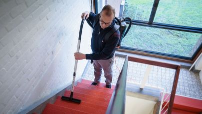 een medewerker van Gom Specialistische Reiniging stofzuigt een trappenhuis van een bewonersflat met een rugstofzuiger