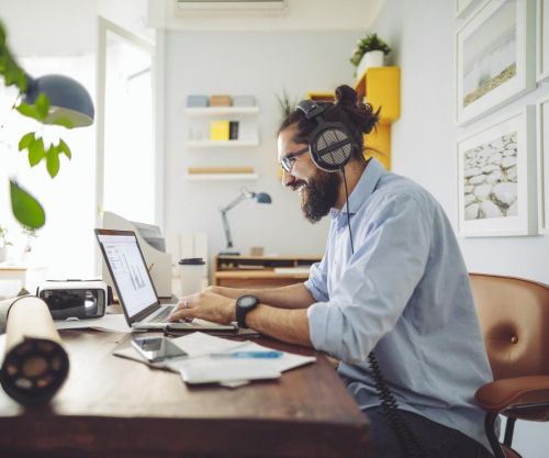 Een man met baard en koptelefoon op zijn oren aan het werk achter een laptop