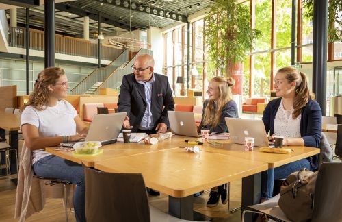 een drietal vrouwelijke studenten zitten aan tafel te studeren en kijken naar de schoonmaakmedewerker van Gom die ze aanspreekt