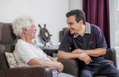 een schoonmaakmedewerker van Gom Zorg maakt een praatje met een bejaarde dame in haar woonkamer