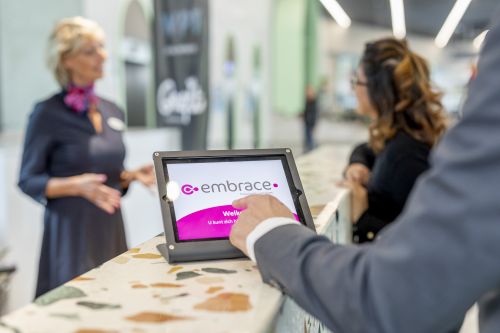 Bezoekers meldt zich aan via de tablet op de balie terwijl de receptioniste in gesprek is met een bezoeker.