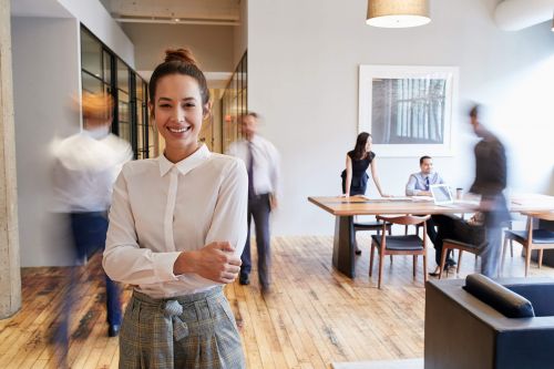 Vrouw staat middenin kantoorruimte waar verschillende collega's langslopen en aan het werk zijn.