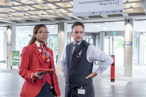 Beveiliger en receptiemedewerker staan naast elkaar en zijn in overleg.