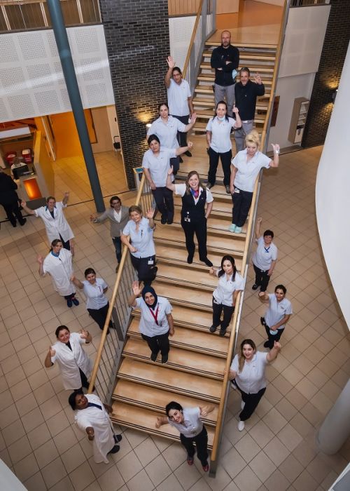 het schoonmaakteam van Gom Zorg bij Deventer Ziekenhuis staan met zijn allen op een trap en kijken omhoog de camera in