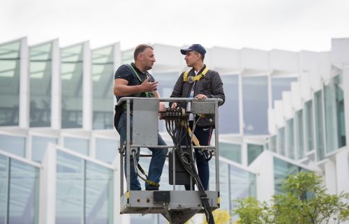 2 mannen staan in het bakje van een hoogwerker en praten met elkaar