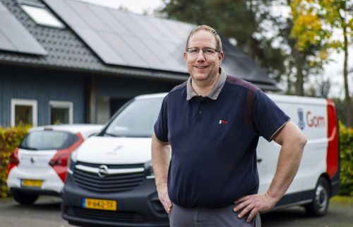 Schoonmaakmedewerker staat met zijn handen in zijn zij voor enkele bedrijfsauto's van Gom