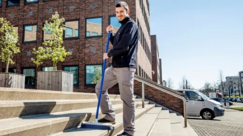 Medewerker van Gom Openbare Ruimten veegt de trappen bij een kantoorpand, symbool voor de uitbreiding met huismeesterdiensten.