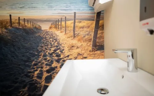 Wastafel in een moderne sanitaire ruimte met een wanddecoratie van een strandpad richting zee, symbool voor rust en ontspanning op het kantoor.