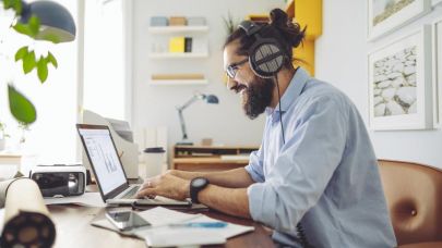 Een man met baard en koptelefoon op zijn oren aan het werk achter een laptop