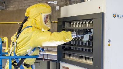 een medewerker van Gom Specialistische reiniging in een geel en geheel afgesloten beschermend pak reinigt een machine bedekt met gevaarlijke stoffen.