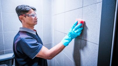 een medewerker van Gom Specialistische Reiniging maakt met een spons de muren van een toilet schoon