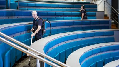 2 medewerkers van Gom Onderwijs maken het auditorium schoon, de een stofzuigt de ander maakt de stoelen schoon