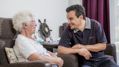 een schoonmaakmedewerker van Gom Zorg maakt een praatje met een bejaarde dame in haar woonkamer