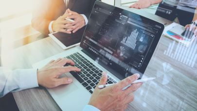 Twee mannen en een vrouw vergaderen aan tafel waarbij je meekijkt op de laptop van één van de mannen wie advies geeft aan de rest van het gezelschap.