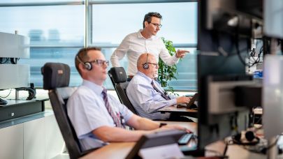 Op de AlarmServiceCentrale bekijken twee mannelijke centralisten de inkomende meldingen op het beeldscherm. Op de AlarmServiceCentrale bekijken twee mannelijke centralisten de inkomende meldingen op het beeldscherm.