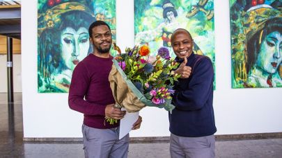 Gom Uitblinker Edman Janga staat, met een bos bloemen in zijn handen, naast een collega die enthousiast zijn duim omhoog doet.