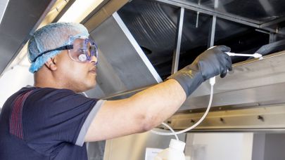 een medewerker van Gom Specialistische Reiniging maakt de binnenkant van een afzuigkap schoon