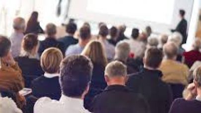 Een zaal vol met mensen in zakelijke kleding die luisteren en kijken naar een presentatie. Een zaal vol met mensen in zakelijke kleding die luisteren en kijken naar een presentatie.