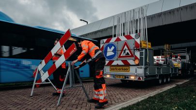 Een verkeersbegeleider in een oranje en blauw uniform plaatst een verkeersrek op de straat.