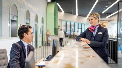 Mannelijke receptionist in uniform zit achter de balie en praat met een gastvrouw in uniform aan de andere kant van de balie.