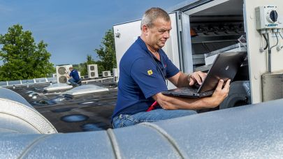 Man aan het werk met zijn laptop bij een ventilatie installatie op het dak.