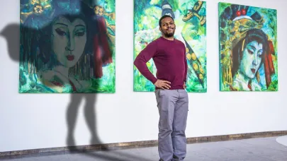 Een portretfoto van Gom Uitblinker Edmar Janga met 3 schilderijen op de achtergrond en een schaduw van een superheld met cape achter Edmar