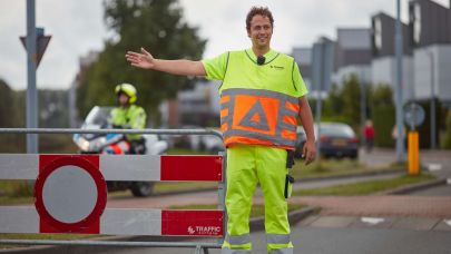 Verkeersregelaar in oranje en geel uniform strekt rechterarm uit en begeleidt het verkeer naar rechts.