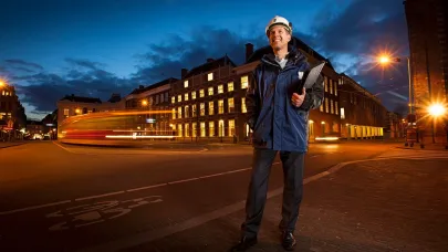 Adviseur van Breijer staat stil op straat en kijkt lachend om zich heen met een map onder zijn linkerarm.