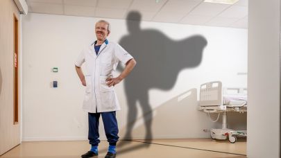 Hans van Rijssel, OK-schoonmaakmedewerker Gom Zorg poseert voor een muur van het ziekenhuis met een bed op de achtergrond en een superheldencape als schaduw achter Hans