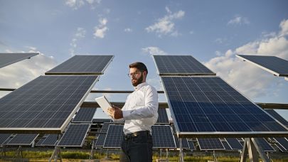 Medewerker energiemanagement analyseert data op tablet staand naast veld met zonnepanelen