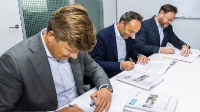 3 personen zitten aan tafel en tekenen een contract