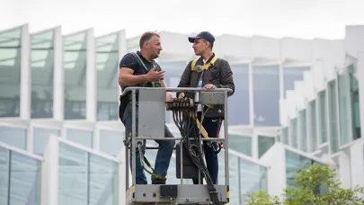 2 mannen staan in het bakje van een hoogwerker en praten met elkaar