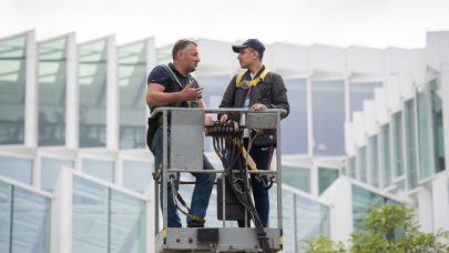 2 mannen staan in het bakje van een hoogwerker en praten met elkaar