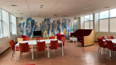 De gerenoveerde ruimte met daarin zit gelegenheden aan tafels en bank.