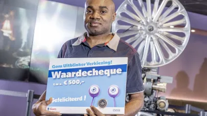 schoonmaakmedewerker Godday Peter staat met een waardecheque in zijn handen voor een filmprojector