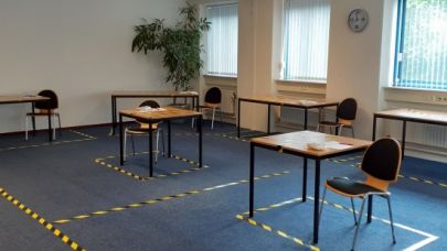 Een leslokaal waar twee bureaus op anderhalve meter afstand zijn geplaatst met daaromheen met lint aangegeven looproutes.
