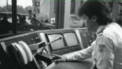 Zwart-wit foto met mannelijke beveiliger achter verouderde computerschermen sprekend in een microfoon. Zwart-wit foto met mannelijke beveiliger achter verouderde computerschermen sprekend in een microfoon.