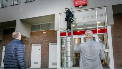 Monteur op een ladder verricht werkzaamheden bij de ingang van een gebouw, terwijl twee mannen beneden toekijken.