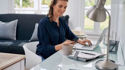 Een vrouw kijkt op haar telefoon terwijl ze achter haar laptop zit te werken