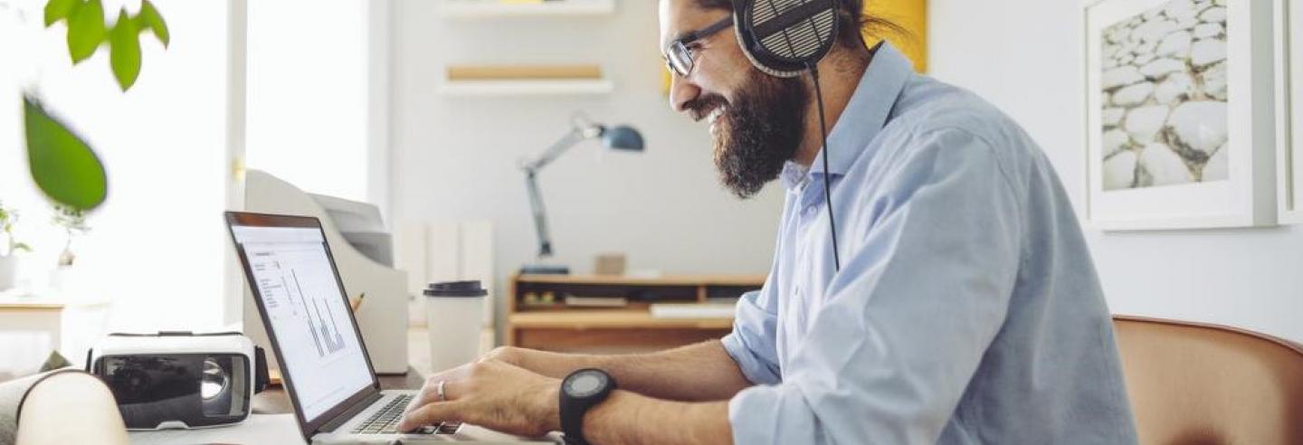 Een man met baard en koptelefoon op zijn oren aan het werk achter een laptop