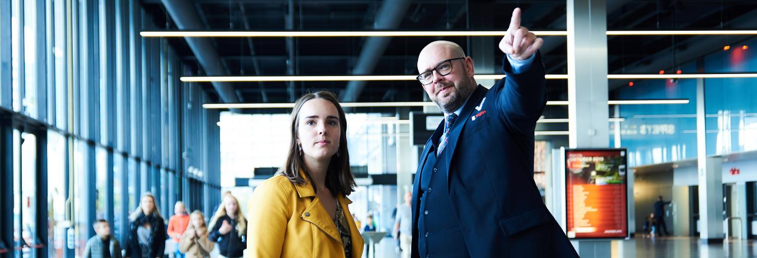 Mannelijke beveiliger in uniform wijst aan een vrouwelijke voorbijganger de weg op Jaarbeurs Utrecht.