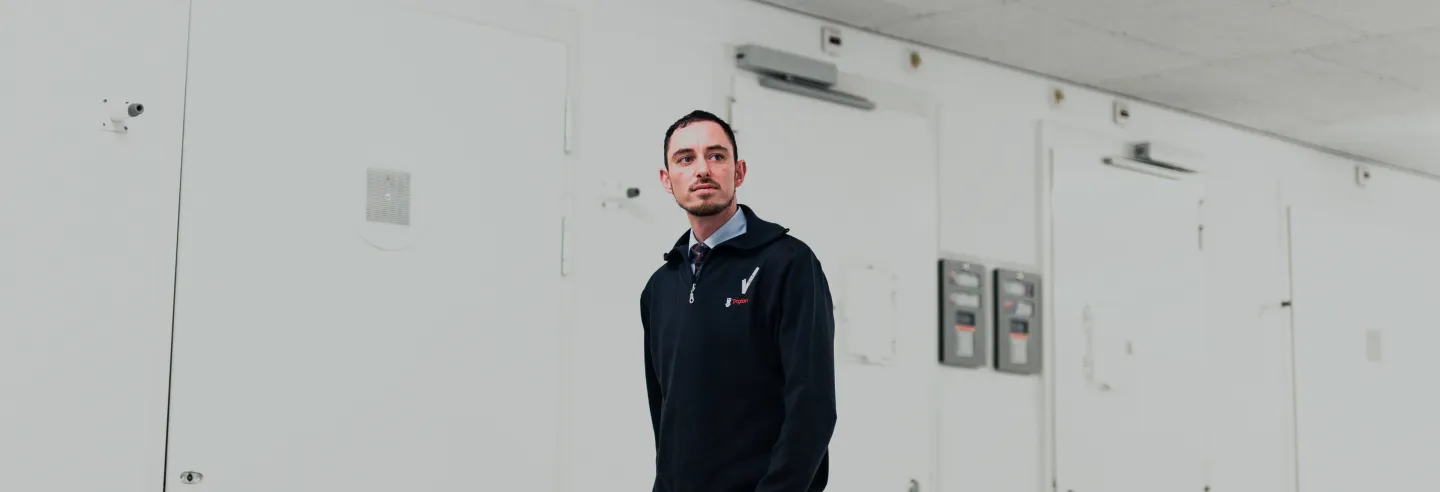 Mannelijke beveiliger loopt op een witte gang met allemaal dichte deuren en controleert op veiligheid.