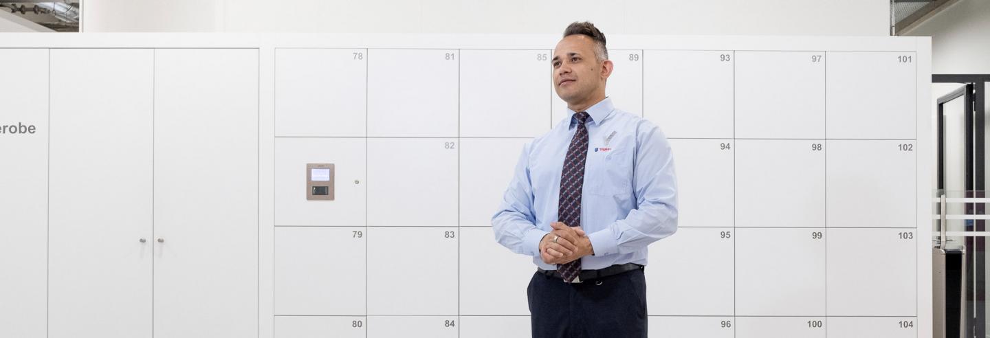 Mannelijke beveiliger staat in de aula van het Albeda College bij de kluisjes geposeerd.