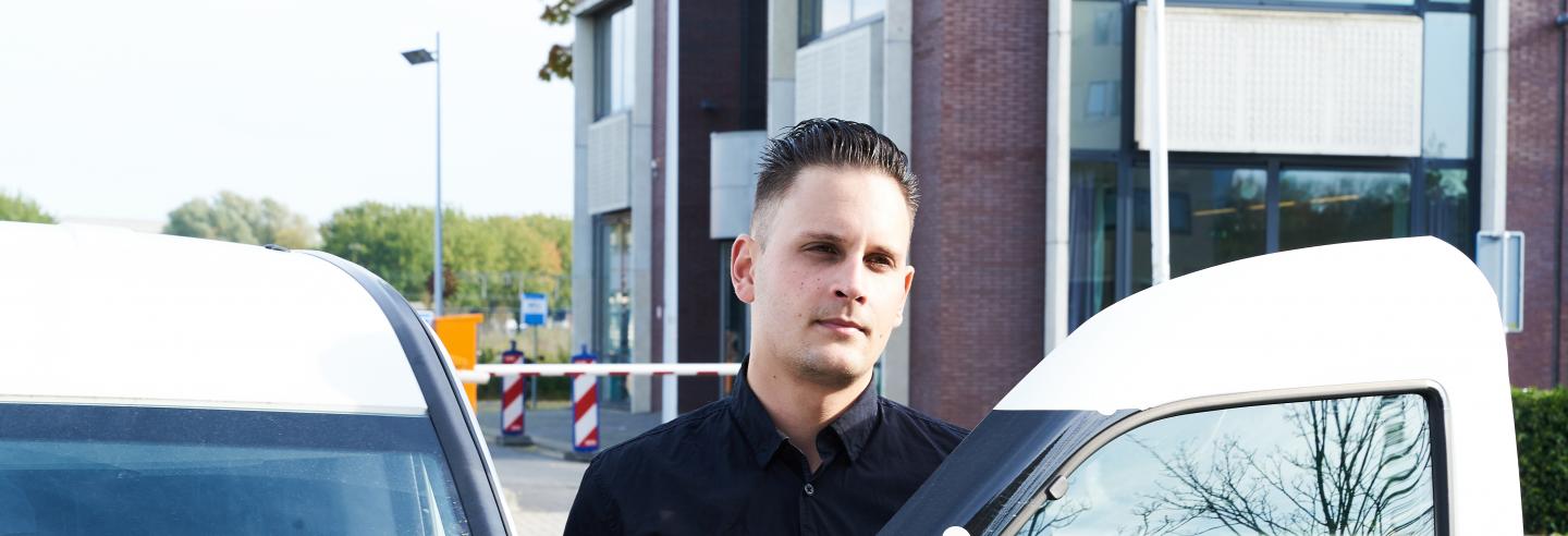 Mannelijke mobiele surveillance medewerker staat bij auto voor een gebouw. De beveiliger staat op het punt om in de auto te stappen en naar de volgende melding toe te rijden.