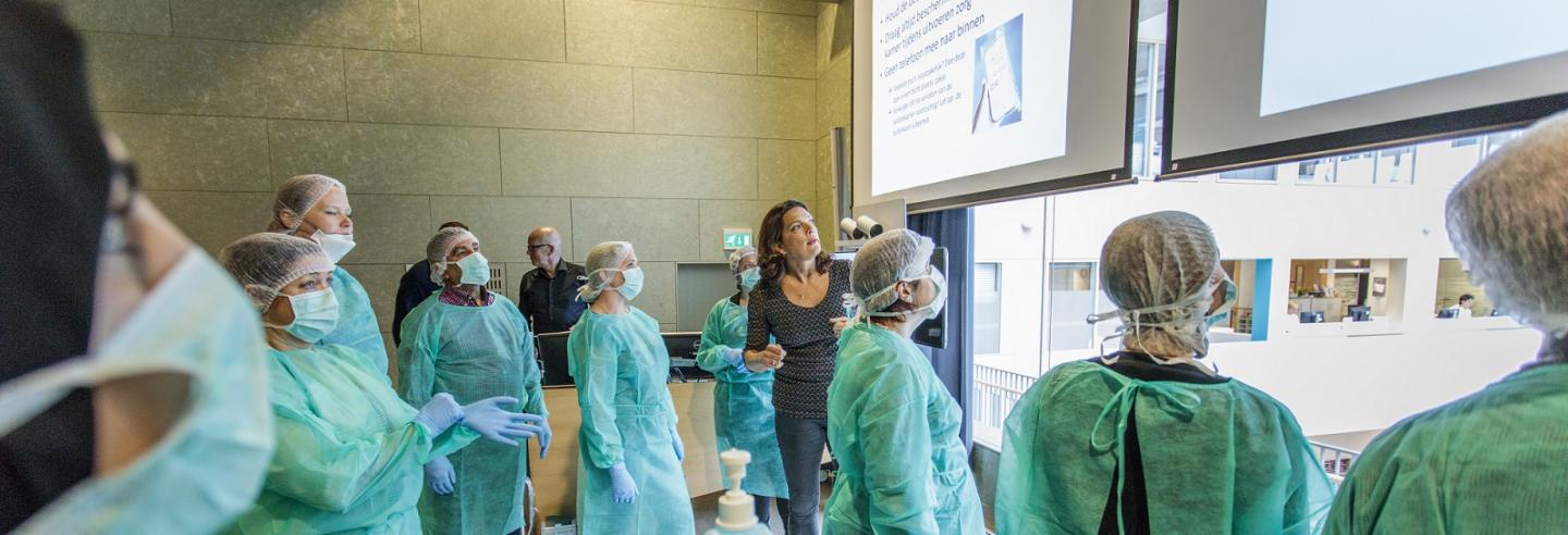 medewerkers van Gom Zorg met beschermkleding aan, schort, mondkapje en haarnetje, luisteren naar docent infectiepreventie