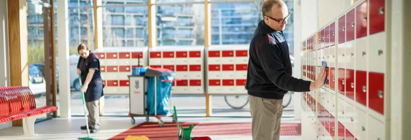 2 medewerkers van Gom Openbare Ruimten maken de entreehal van een flat schoon, de een wist de vloer de ander het postvakjestableau