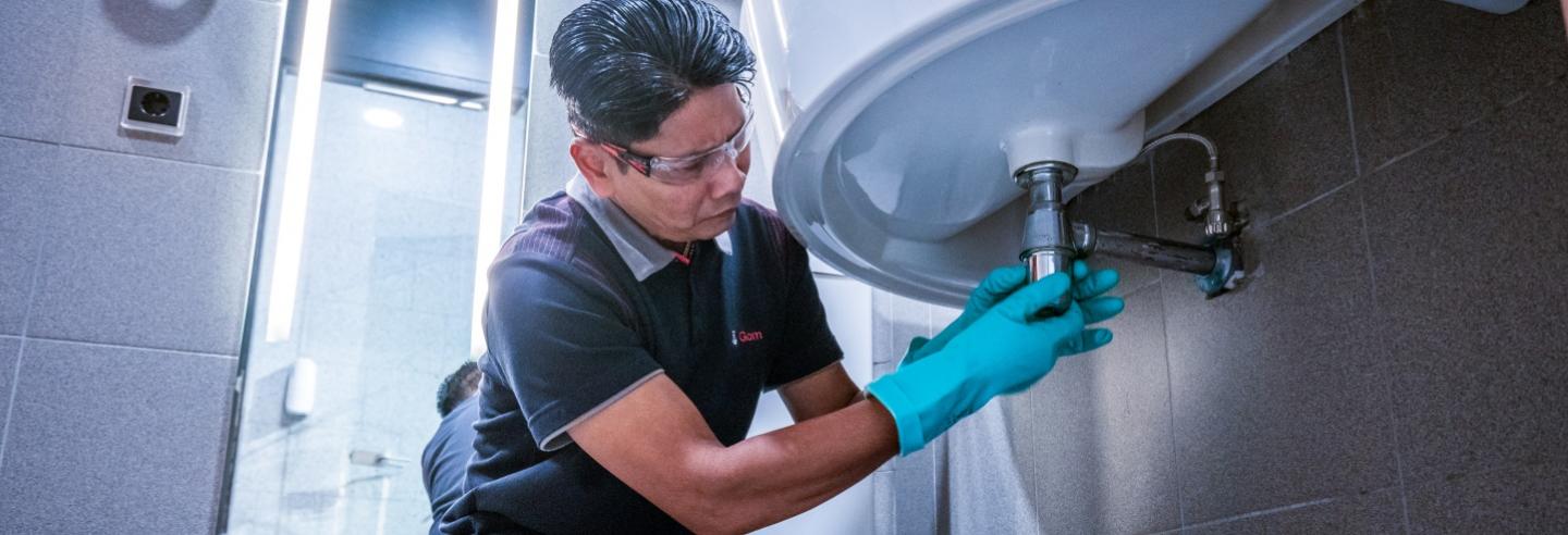 een medewerker van Gom Specialistische Reiniging maakt het sifon van een wastafel schoon tijdens een dieptereiniging sanitair