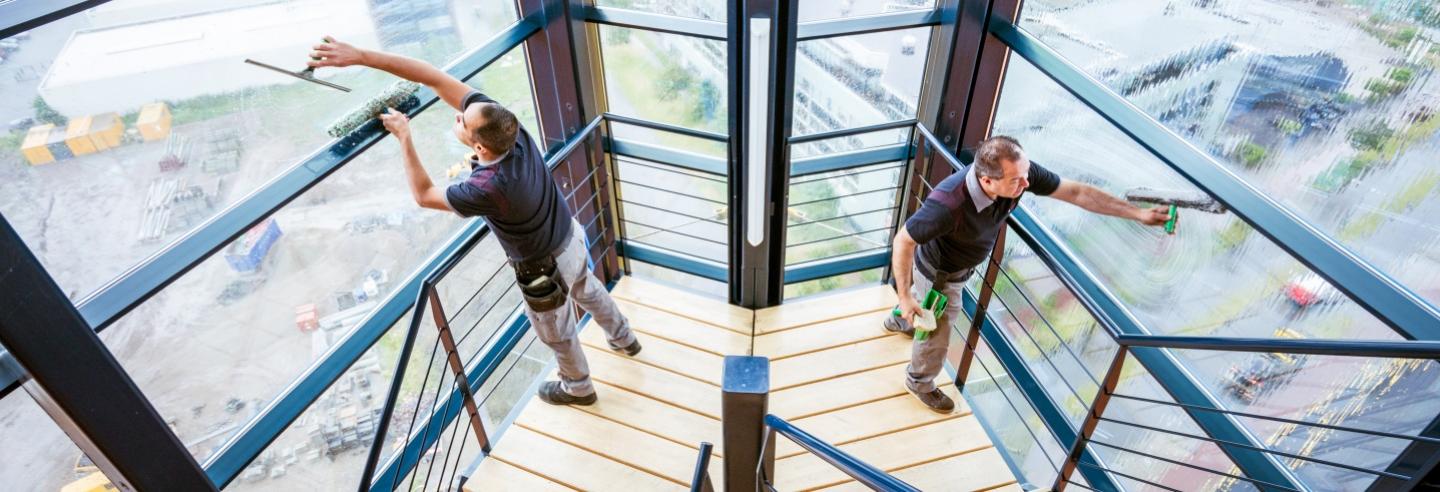 2 medewerkers van Gom Specialistische Reiniging zemen de ramen in een trappenhuis met hele hoge ramen