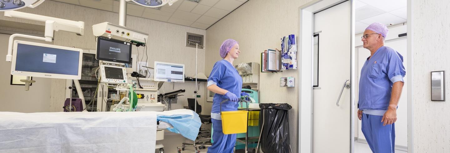 een schoonmaakmedewerkster van Gom loopt de operatiekamer uit terwijl de chirurg naar binnen loopt